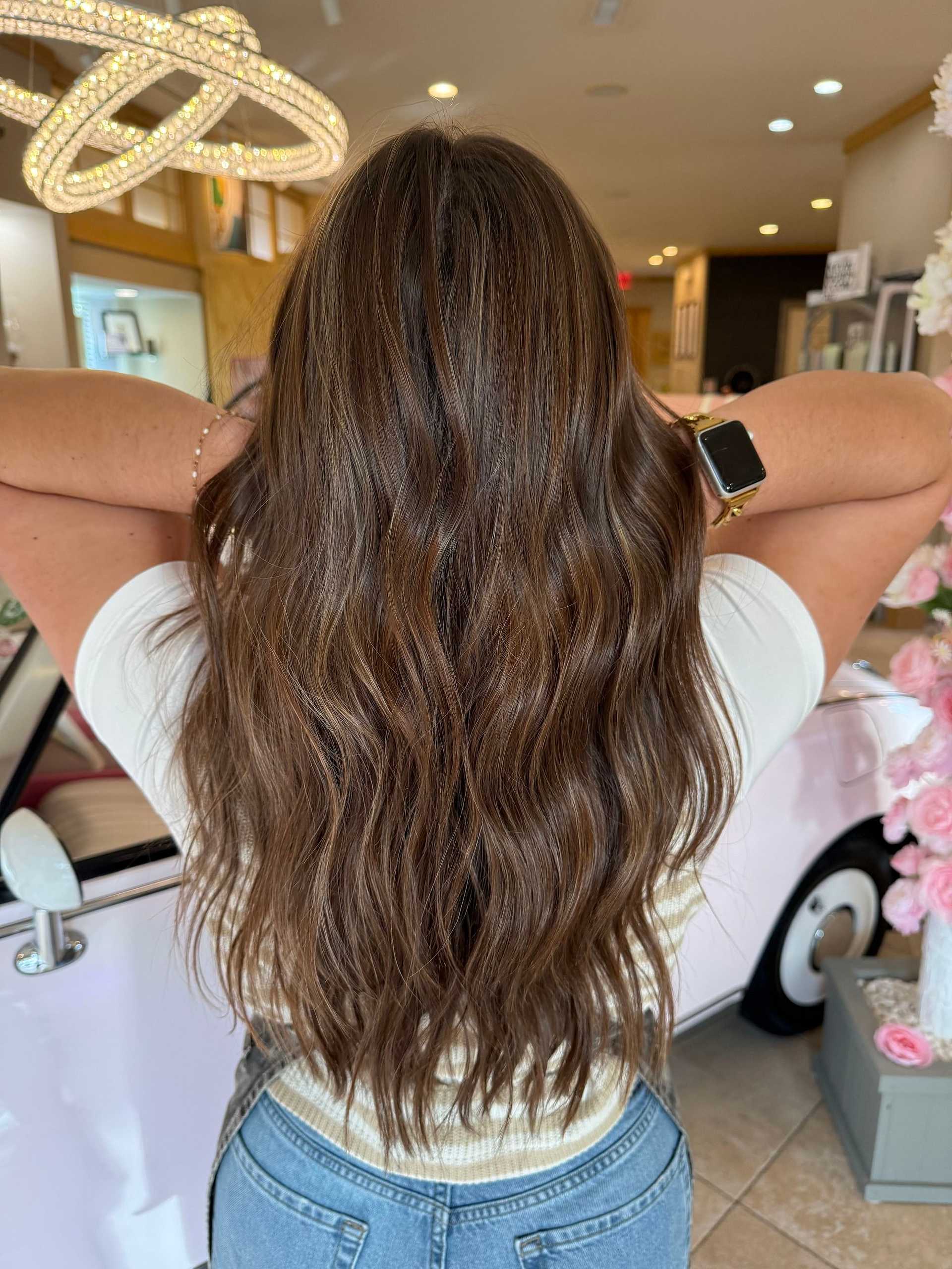 Long wavy brunette hair with subtle highlights, styled in a salon setting.